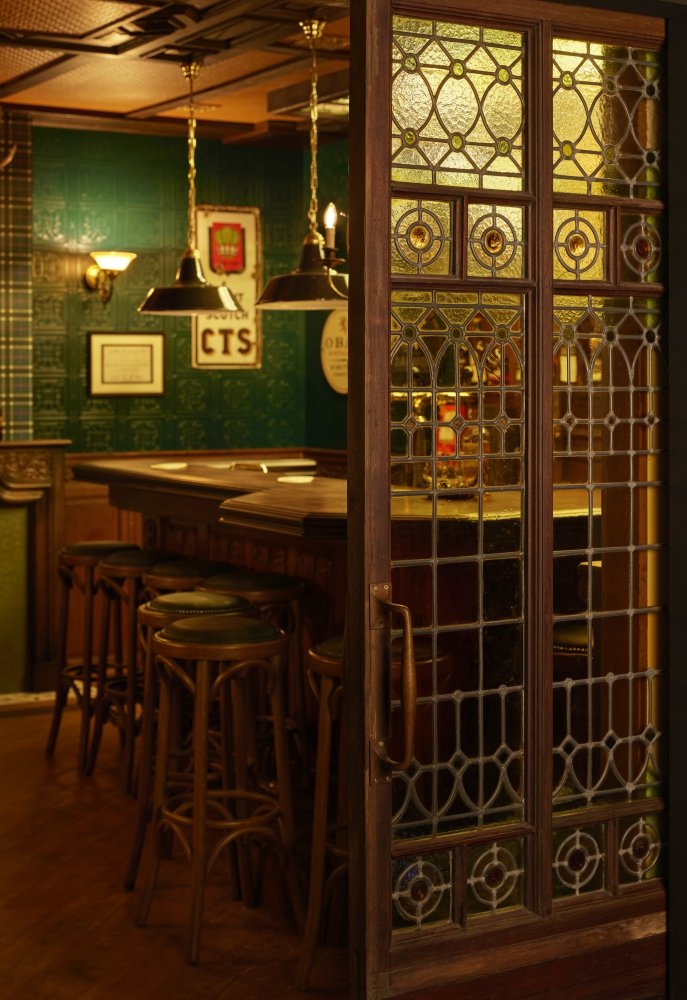Hergebruikte schuifdeur met glas-in-lood, gezien vanaf de thuisbioscoop met op de achtergrond het interieur van de Ierse Pub.