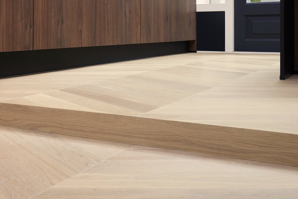 Detailfoto van een houten vloer die op deze manier eenheid vormt tussen de eetkamer en de (uitgebouwde) keuken.